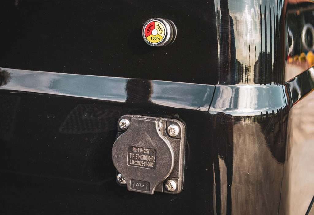 Close-up of a vehicle's rear with a round emblem and a charging port labeled 'Electric Vehicle'.