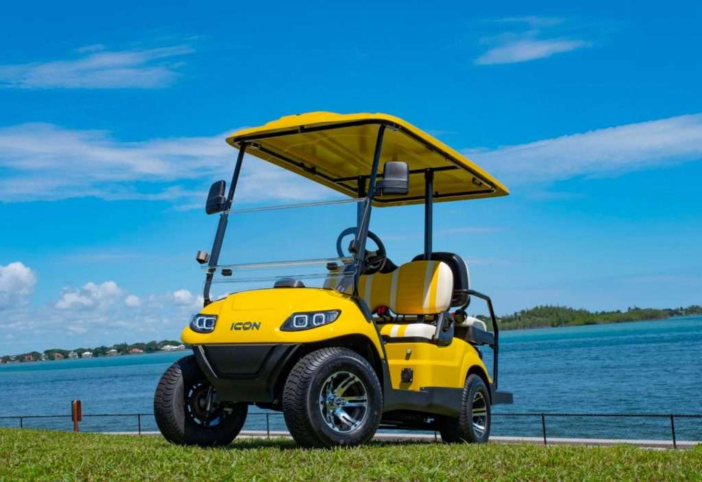 A yellow golf cart parked on a green field under a blue sky.