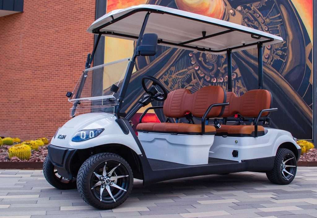 White golf cart with brown seats parked near a mural wall.