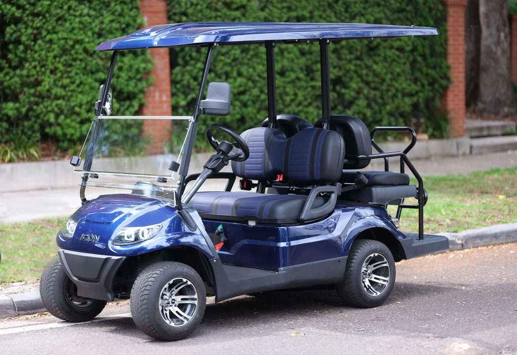 A blue golf cart parked near a green hedge.