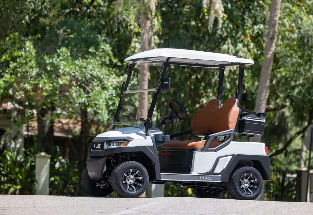 A white golf cart parked outdoors with greenery in the background.