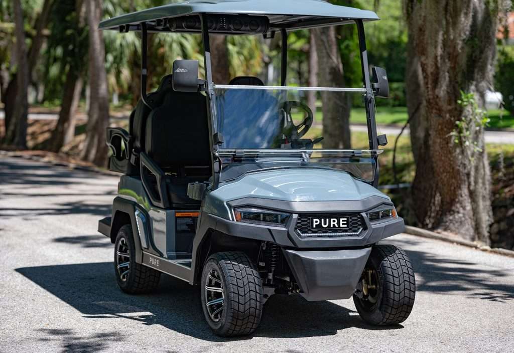 A black golf cart parked on a paved path surrounded by trees.