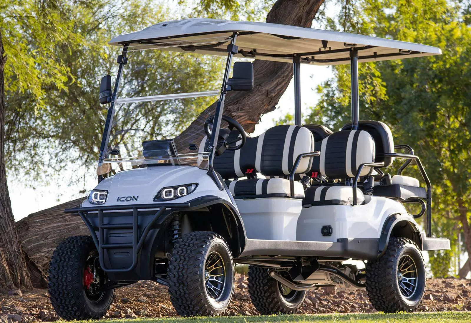 A white golf cart parked outdoors under a tree.