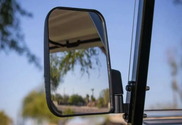 Side mirror reflecting a blurred outdoor scene on a sunny day.