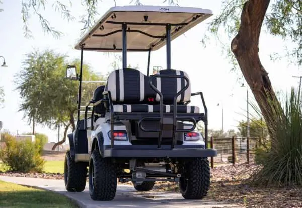 A black and white golf cart parked on a dirt path under trees.