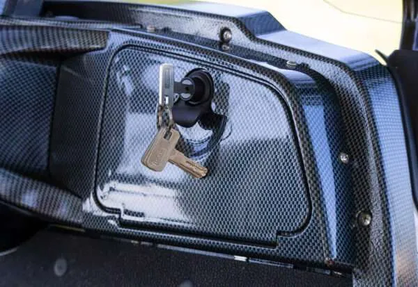 Car trunk lock with keys inserted on a carbon fiber surface.