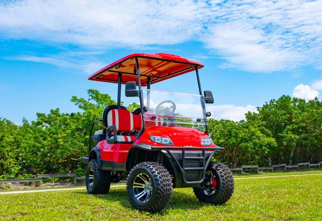 Red golf cart parked on a green lawn under a blue sky.