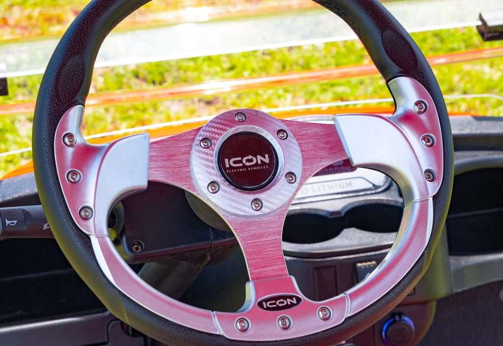 Close-up of a sleek metallic car steering wheel with a vibrant yellow dashboard.