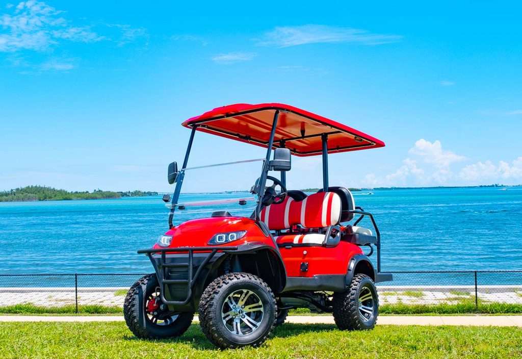 A red golf cart parked near a waterfront on a sunny day.