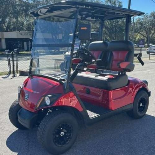 Red golf cart with black roof and lifted wheels parked outside.